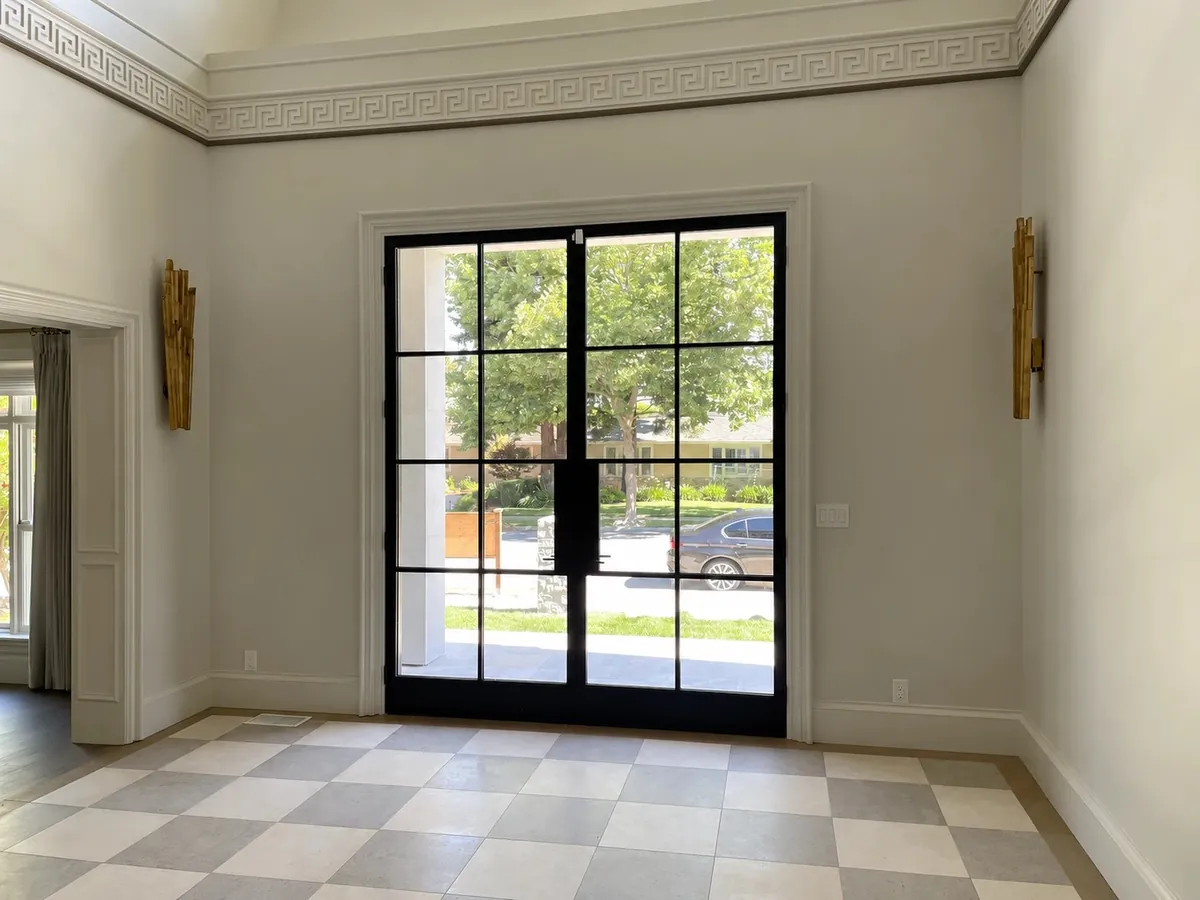 Double-height entry with steel-framed glass doors, a Greek-key cornice, gold sconces and a checkerboard stone floor