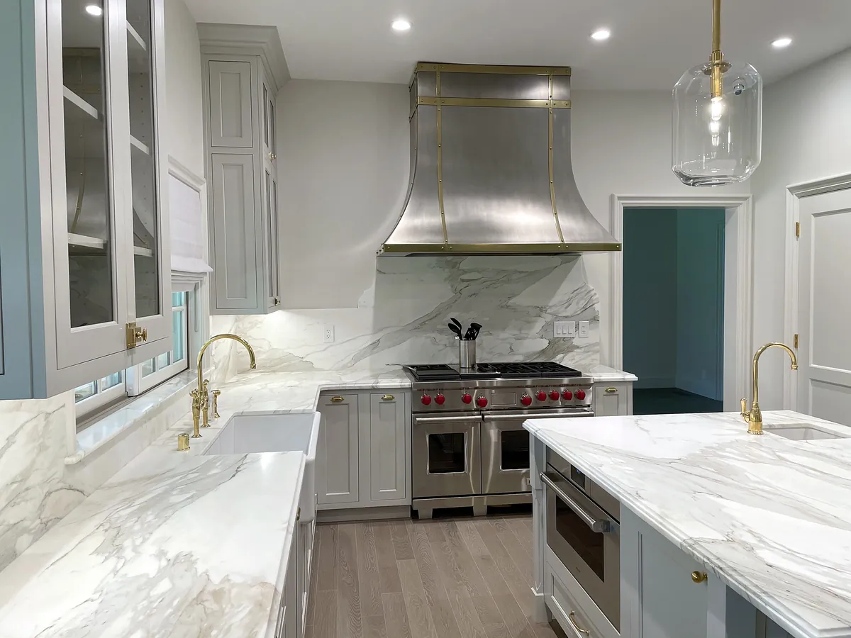 Kitchen with a brass-trimmed range hood, marble backsplash and glass-front cabinets