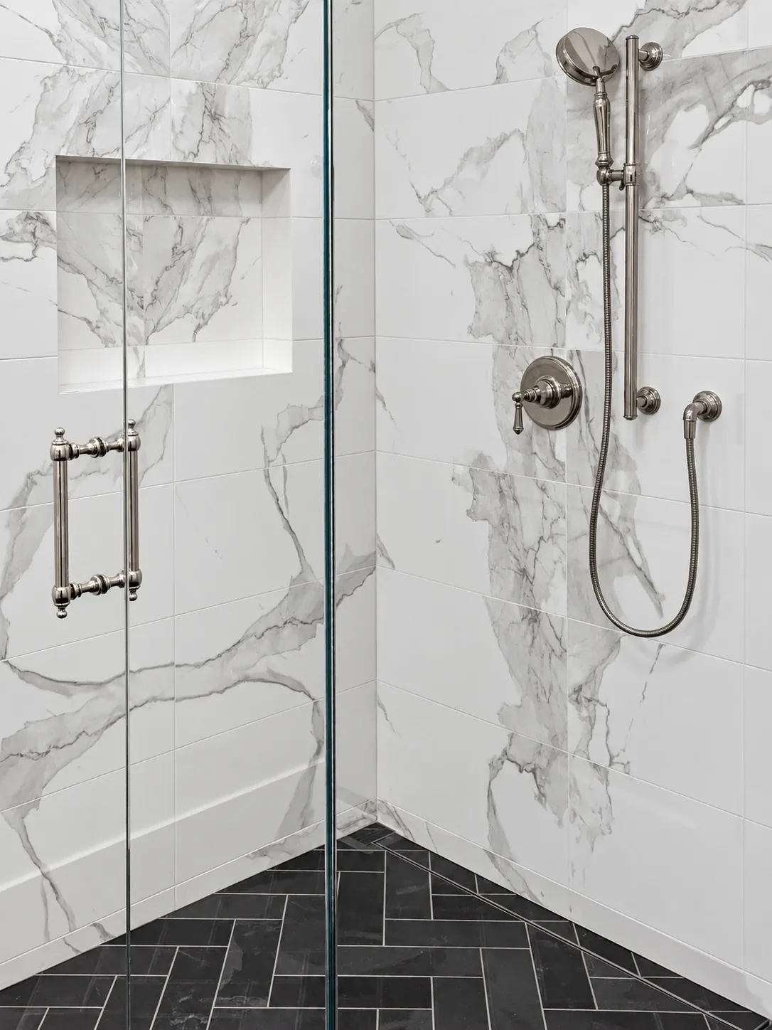 Glass shower with large marble-look wall tile, a recessed niche, polished-nickel fixtures and a charcoal herringbone floor