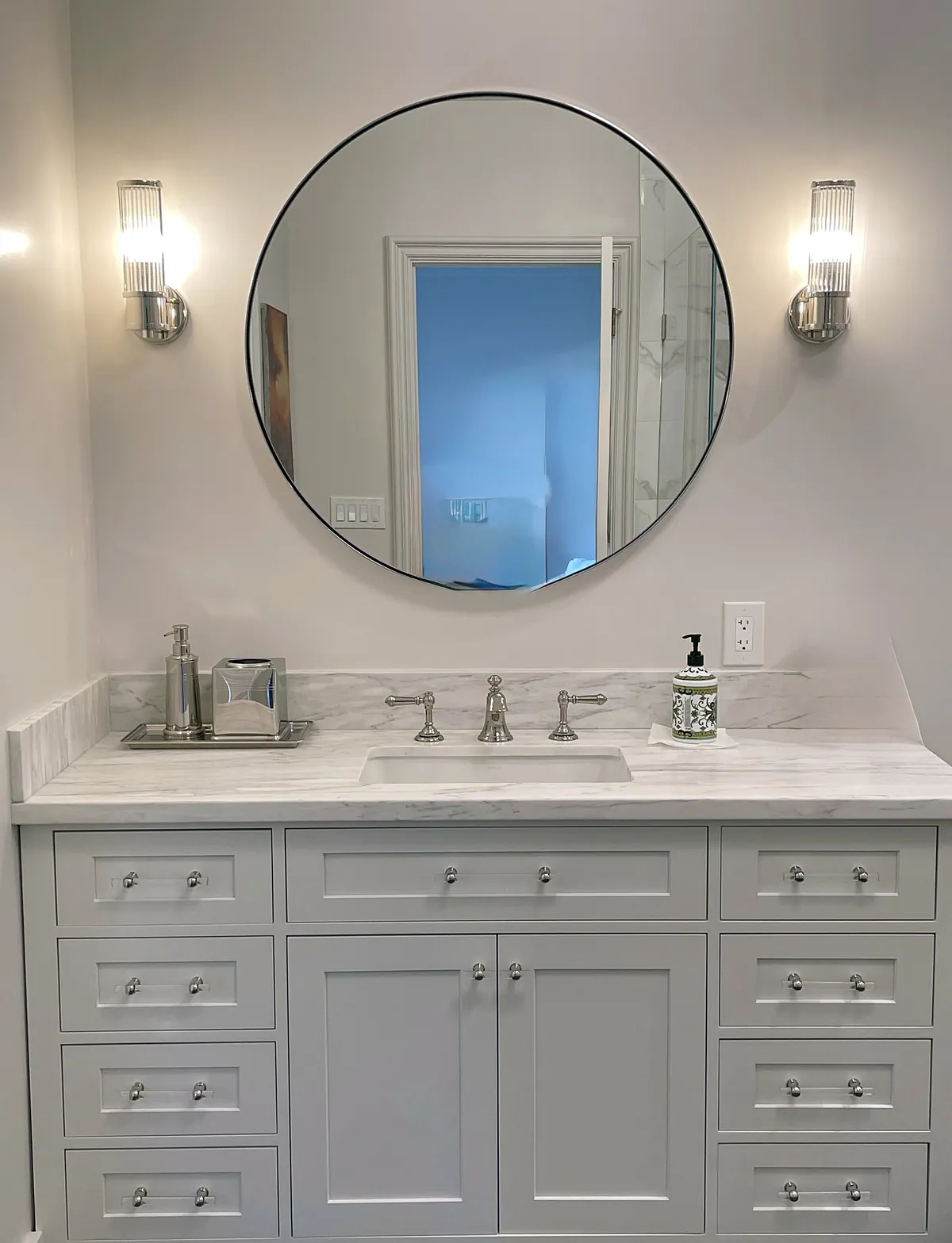 Bathroom vanity with marble top, round mirror and sconces