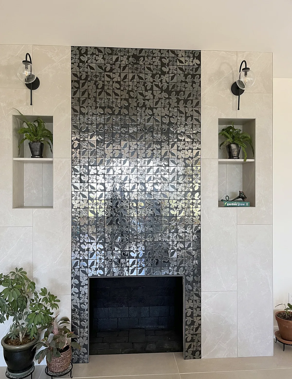Fireplace wall with a floor-to-ceiling metallic mosaic surround, tiled niches and black sconces